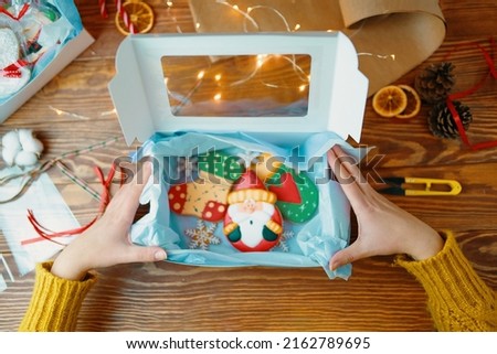 Girl's hands open gift box with Christmas cookies. Gingerbread with icing. Festive sweets for children in form of santa claus, mittens, socks and snowflakes. New Year's composition on wooden table.