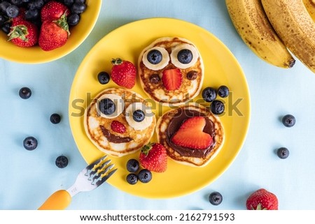 American pancakes decorated like smile and happy faces with strawberries, chocolate, blueberries and banana. Food for kids, playful and creative. Top view. Royalty-Free Stock Photo #2162791593