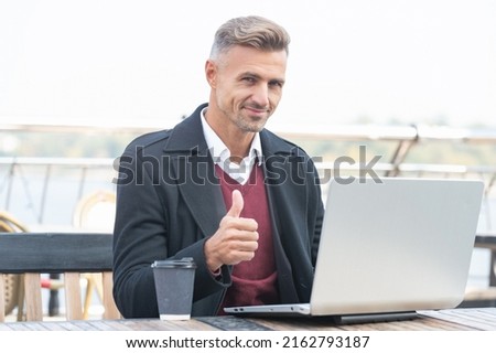 Happy professional man give thumb making approval gesture working in laptop in outdoor cafe
