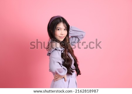 The cute young Asian woman with preppy dressed standing on the pink background.