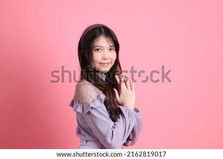 The cute young Asian woman with preppy dressed standing on the pink background.