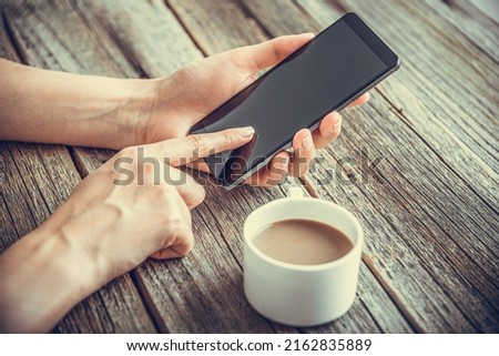 Smartphone in hands on the background of a wooden table and a cup of coffee.