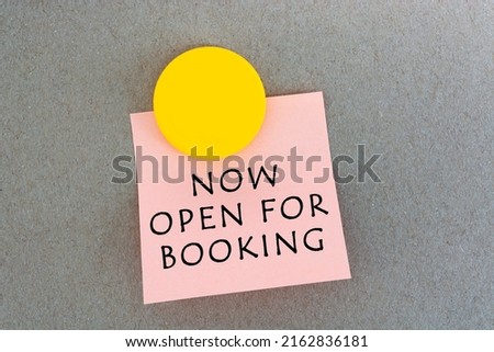 Now open for booking text on sticky notes with yellow smile face magnet. Directly above. Flat lay.