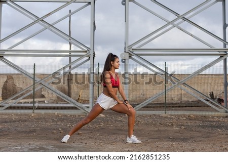 Female young athlete warming up before running outdoor on industrial zone. Sporty fit woman training outside.