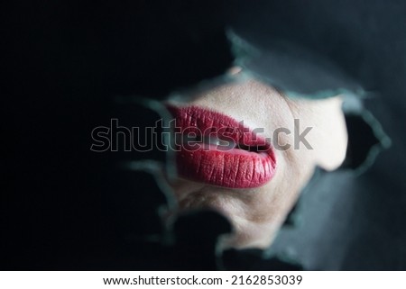 lips with red lipstick seen through a torn hole of black paper for concept