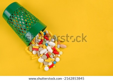 A lot of expired pills and medicines are poured out of the green urn on a yellow background.The concept of waste medicines is to collect for recycling.The National Prescription Drug Goes Back A Day. Royalty-Free Stock Photo #2162853845