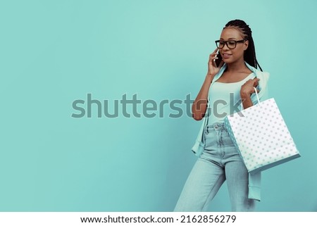 Monochrome portrait of young charming girl with afro hairdo holding shopping bag using phone isolated on blue background. Concept of beauty, art, fashion, youth, sales and ads.Copy space for ad