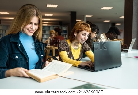 Young university students using laptop and reading book in library - School education concept