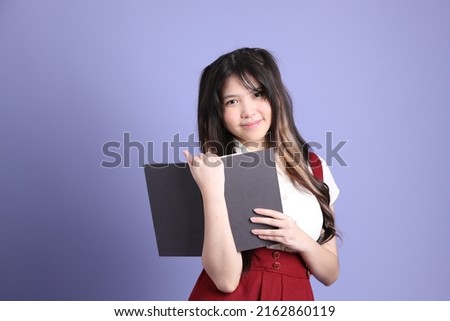 The cute young Asian woman with preppy dressed standing on the purple background.