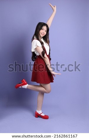 The cute young Asian woman with preppy dressed standing on the purple background.