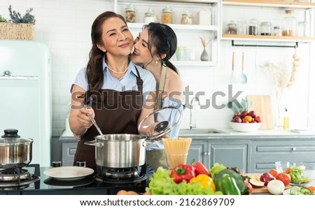 daughter hug and kiss mother. Asian family making food in kitchen at home together.