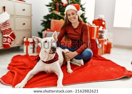 Young caucasian woman smiling confident sitting with dog by christmas tree at home