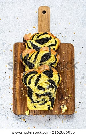Unusual pumpkin marbled (tiger print) bread with cuttlefish ink, braided on a wooden board on a light background. Useful home baking.