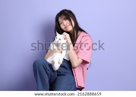 The cute young Asian girl with casual clothes sitting on the purple background.