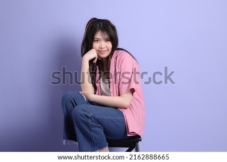 The cute young Asian girl with casual clothes sitting on the purple background.