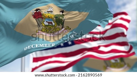 Delaware state flags waving along with the national flag of the United States of America. In the background there is a clear sky. Royalty-Free Stock Photo #2162890569