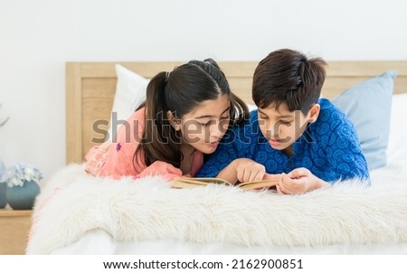 Indian teenage adorable boy, girl sibling laying down on bed, playing, reading book and doing homework together with fun and happiness at cozy home in a day. Lifestyle, Family, Education Concept Royalty-Free Stock Photo #2162900851
