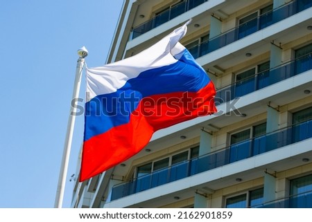 The flag of Russia is flying against the background of the building, close-up
