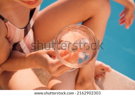 Young charming  woman chilling near swimming pool and drinking rose wine at sunset. Luxury lifestyle content. Top view picture.