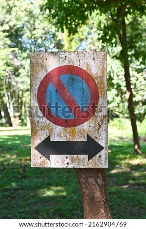 Old wooden traffic sign painted in white with a red circle symbol on a blue background (red line 45 degree angle) was installed in the garden. Symbol indicates that parking of any kind is prohibited, 