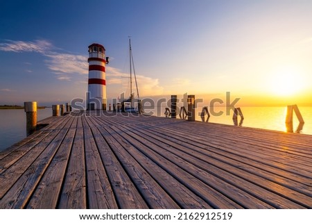 Lighthouse at Lake Neusiedl, Podersdorf am See, Burgenland, Austria. Lighthouse at sunset in Austria. Wooden pier with lighthouse in Podersdorf on lake Neusiedl in Austria. Royalty-Free Stock Photo #2162912519