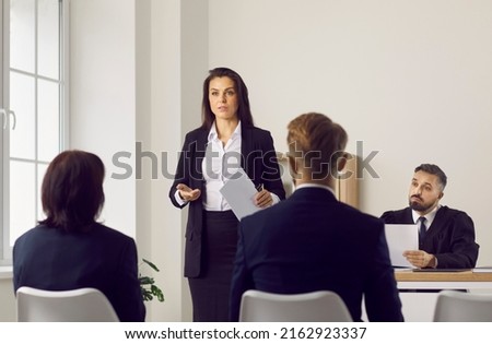 Serious woman who is defense lawyer representing defendant or plaintiff attorney representing suing party in criminal prosecution is standing in courtroom during court trial and speaking to audience Royalty-Free Stock Photo #2162923337