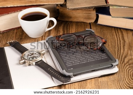 E-book, coffee and stacks of paper books. Atmosphere of reading and learning.