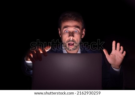 Businessman staring at laptop with frightened face in the dark Royalty-Free Stock Photo #2162930259