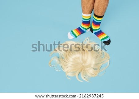 Minimal shot of man wearing rainbow socks with blond wig on floor at pastel blue background, copy space Royalty-Free Stock Photo #2162937245