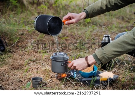 A tourist pours hot water from a pot into a pot, cooks food in the camp, breakfast on a hike through the forest, brews food with hot water, pours liquid. human hands. High quality photo