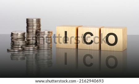 ICO. wooden cubes. blocks lie on a black background. stacks with coins. inscription on the cubes is reflected from the surface of the table. ICO - short for Initial Coin Offering