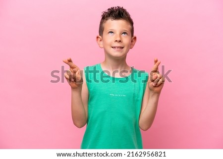 Little caucasian boy isolated on pink background with fingers crossing and wishing the best