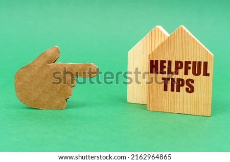 Business real estate concept. On a green surface, a hand points to a house with an inscription - Helpful Tips