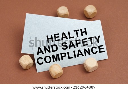 The concept of industrial safety. On a brown surface, wooden cubes and a business card with the inscription - Health and Safety Compliance