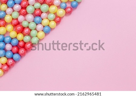 Multi-colored round glossy balls of sugar confectionery lie diagonally to the left on a pink background.