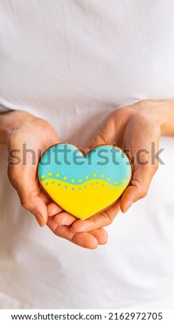 Close-up of Woman hands hold heart shape gingerbread cookie with ukrainian flag colors