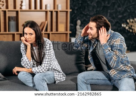 Clarification of relations between spouses. Caucasian couple sitting on sofa in living room, quarreling over disagreement, man yelling at woman, woman experiencing psychological abuse from her husband Royalty-Free Stock Photo #2162982865