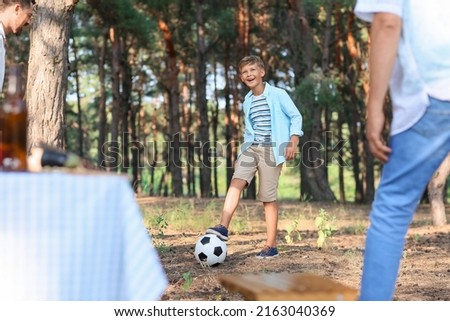 Little boy playing soccer with his father and grandfather in forest