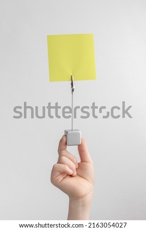 child hand holding yellow blank reminder or paper notes above a white and gray background, copy space