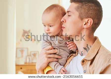 Close-up, a young handsome caucasian father holds in his arms a little son, a newborn, an infant, in a bright children's room. Father and son spend time together, happy family moment.