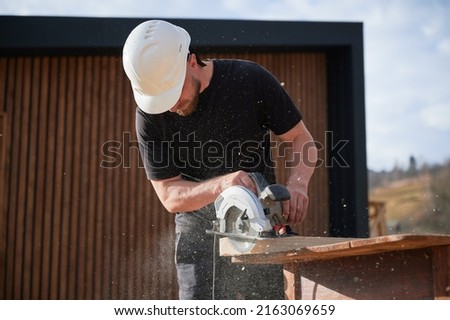 Carpenter using circular saw for cutting wooden plank. Man worker building wooden frame house. Carpentry concept. Royalty-Free Stock Photo #2163069659