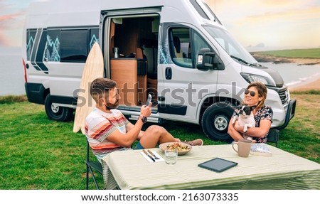 Young man taking photo to happy woman hugging lovely dog with camper van and beach on background