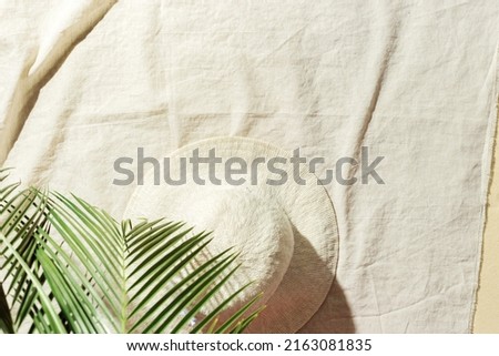 Summer minimal background, top view wide-brimmed sun hat under palm leaf on beach towel on sand. Summer aesthetic photography pastel beige colored, copy space, vacation, relaxation concept. Above view