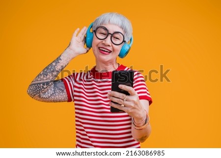 old senior asian female listening music headphone and smartphone  while move dance positive carefree emotion isolated on yellow background,asia woman with tattoo happy music dance sing studio shot