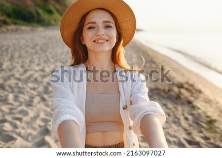 Close up young smiling satisfied happy tourist traveler woman 20s wearing white clothes hat doing selfie shot pov on mobile phone at sunrise over sea beach ocean outdoor seaside in summer day evening
