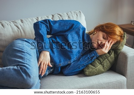 Young sick woman with hands holding pressing her crotch lower abdomen. Medical or gynecological problems, healthcare concept. Young woman suffering from abdominal pain while laying on sofa at home Royalty-Free Stock Photo #2163100655