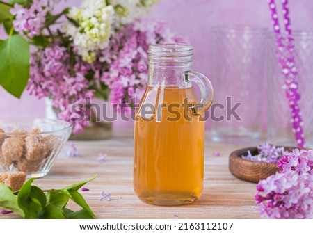 Lilac flavored sugar syrup for lemonades, ice cream or biscuits in a glass bottle on a light wooden background. Natural flower ingredients for cooking.