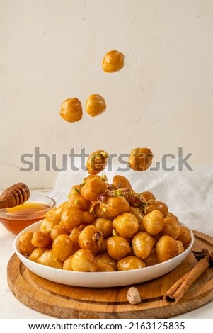 luqaimat fried dough balls in sweet honey syrup, traditional dessert, food levitation. White plate. Royalty-Free Stock Photo #2163125835