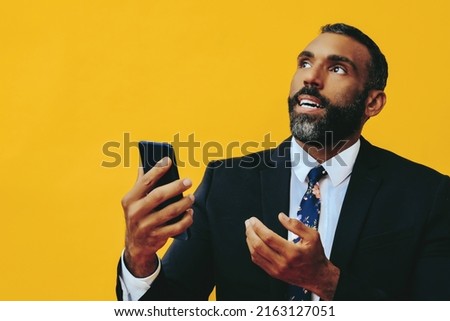 portrait of anxious stressed expressive bearded gentleman in suit and tie with smartphone video call hand up yellow background studio