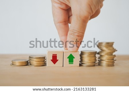 businessman's hand choose green arrow up sign on wooden cube block with stack of coins